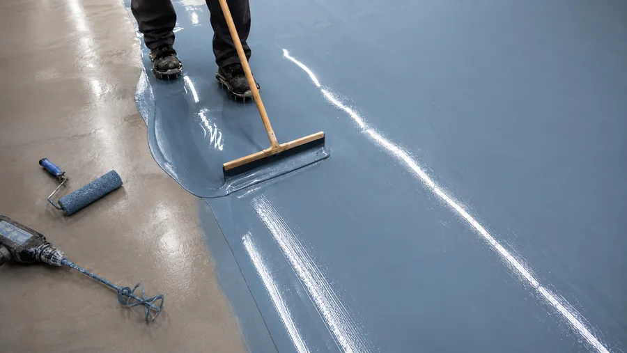 Installer in spiked shoes pulling a squeegee through freshly poured slate-blue floor coating